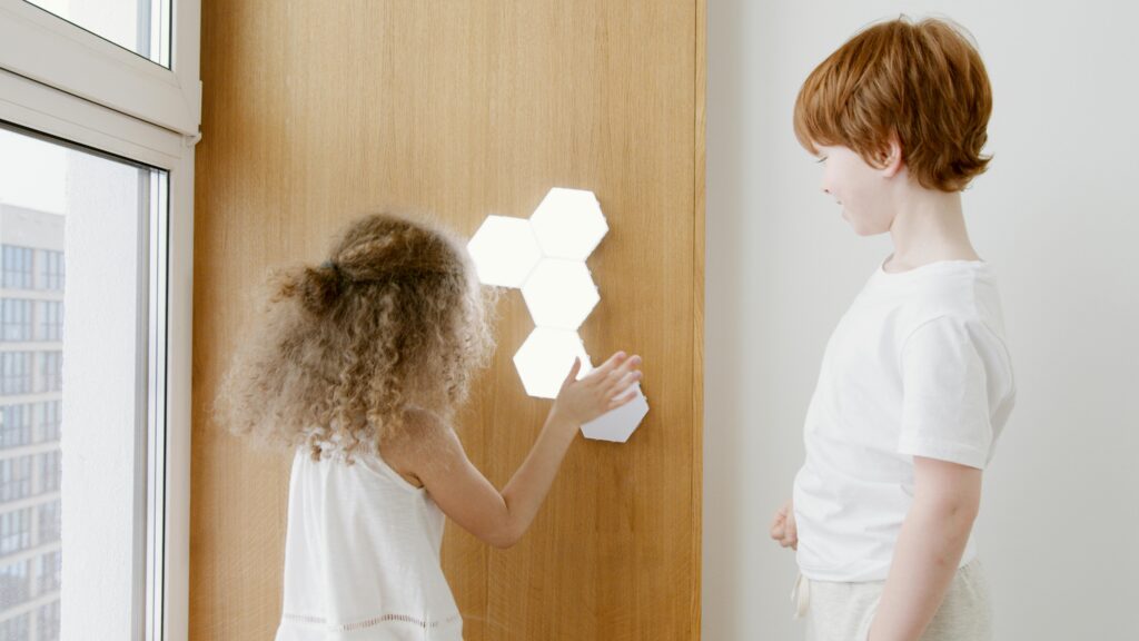 Two kids engage with hexagonal LED wall lights indoors.