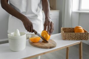 An adult slicing fresh oranges on a wooden chopping board in a bright kitchen setting.