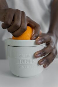 Detailed close-up showing hands squeezing an orange in a manual juicer.