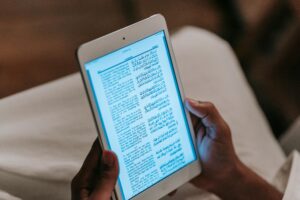 Crop unrecognizable person in casual clothes reading text on tablet against blurred background in room