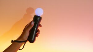 Close-up of a hand holding a VR motion controller with a glowing light against a gradient background.