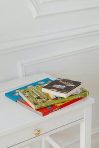 Vertical shot of children's books stacked on a white table in a bright space.