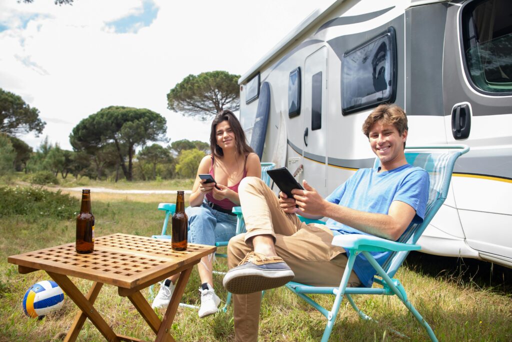 A couple relaxing outside their campervan with gadgets in a scenic countryside setting.
