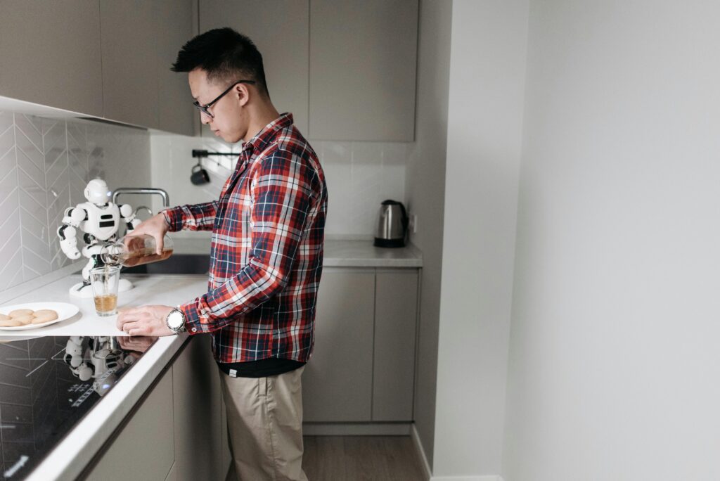 Man in plaid shirt pours drink in a sleek kitchen with a robot.
