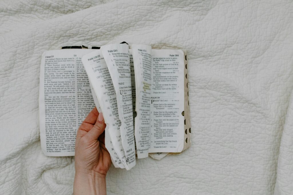 A hand gently holds an open Bible, showcasing its pages on a white fabric background.