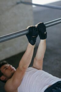 Adult male performing pull-ups indoors with gloves for fitness and strength training.