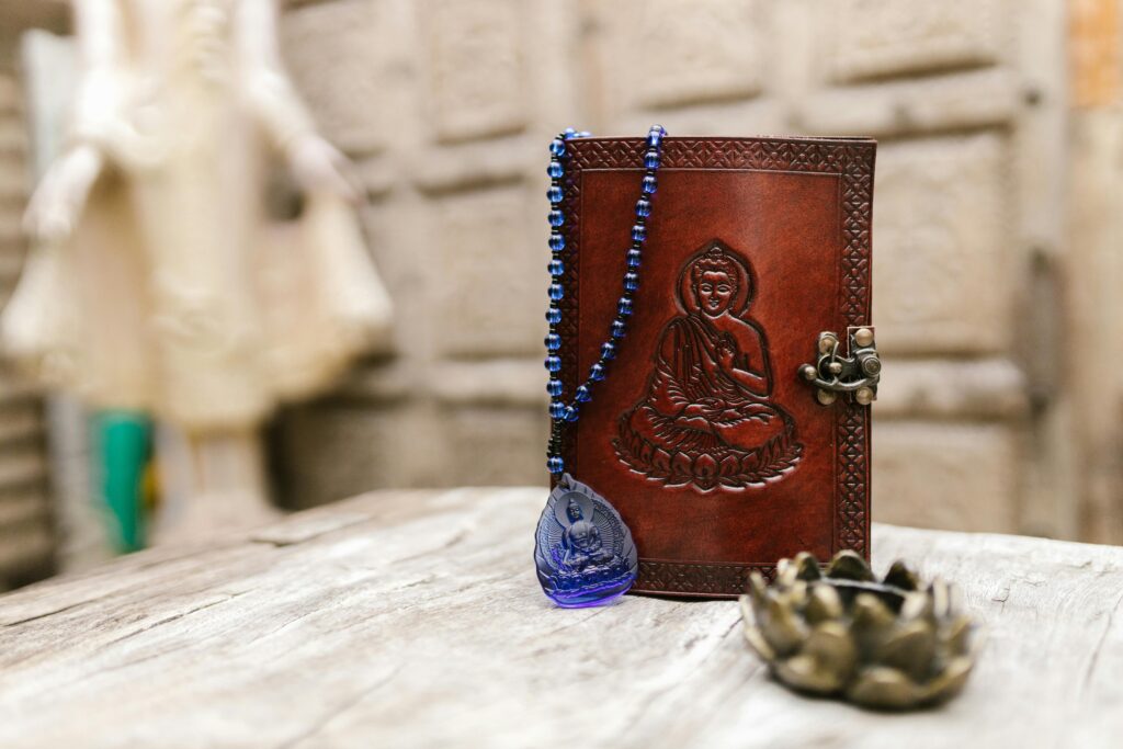 A close-up of a leather journal embossed with Buddha and a blue beaded necklace, symbolizing spirituality.