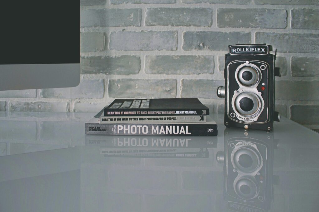 A vintage Rolleiflex camera beside photography books on a reflective surface indoors.