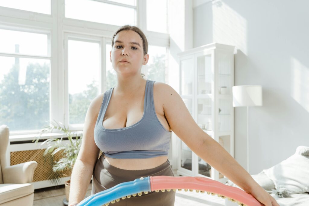 Plus-size woman in activewear exercising with a hoop indoors. Bright, modern setting.
