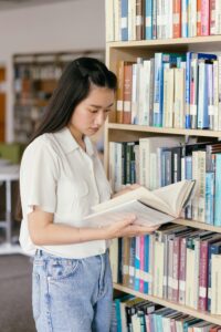 An Asian woman reading a book in a library, focused on learning.