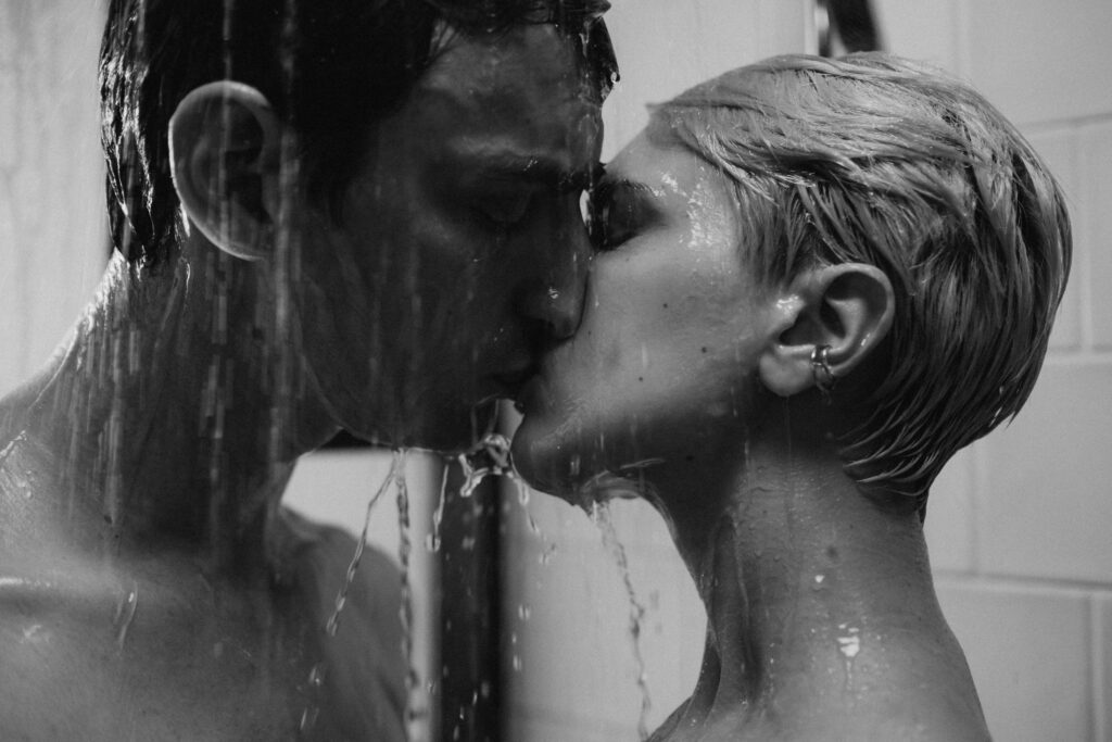 Intimate grayscale image capturing a couple kissing passionately in a shower.