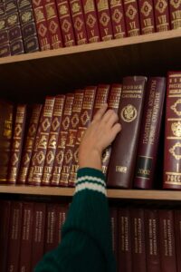 A hand reaches for a red book on a neatly organized bookshelf in a library setting.