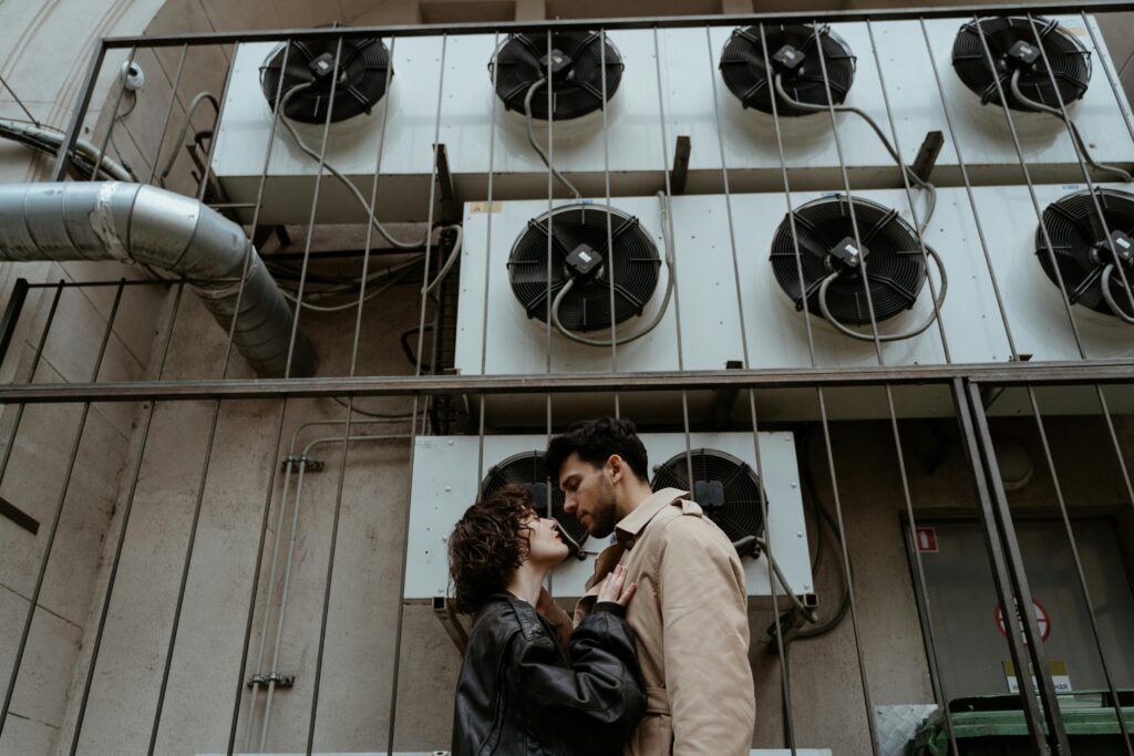 A stylish couple shares an intimate moment near industrial air conditioning units.