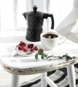 A black moka pot and coffee cup on a rustic chair with raspberries creating a cozy setting.