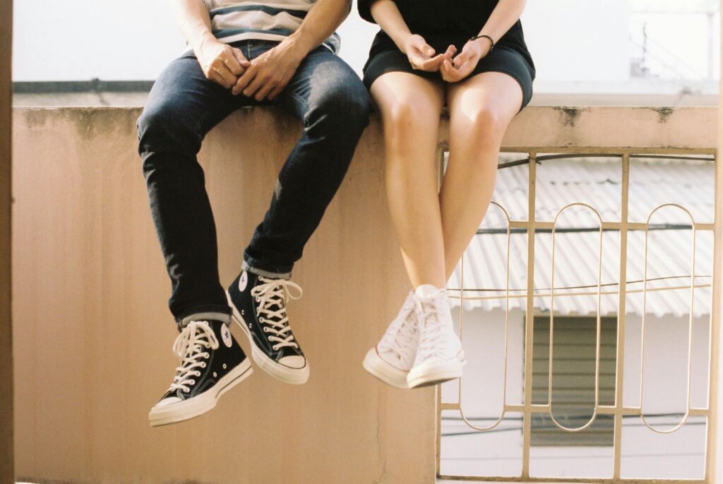 A relaxed couple sitting on a ledge, wearing stylish sneakers, showcasing togetherness.