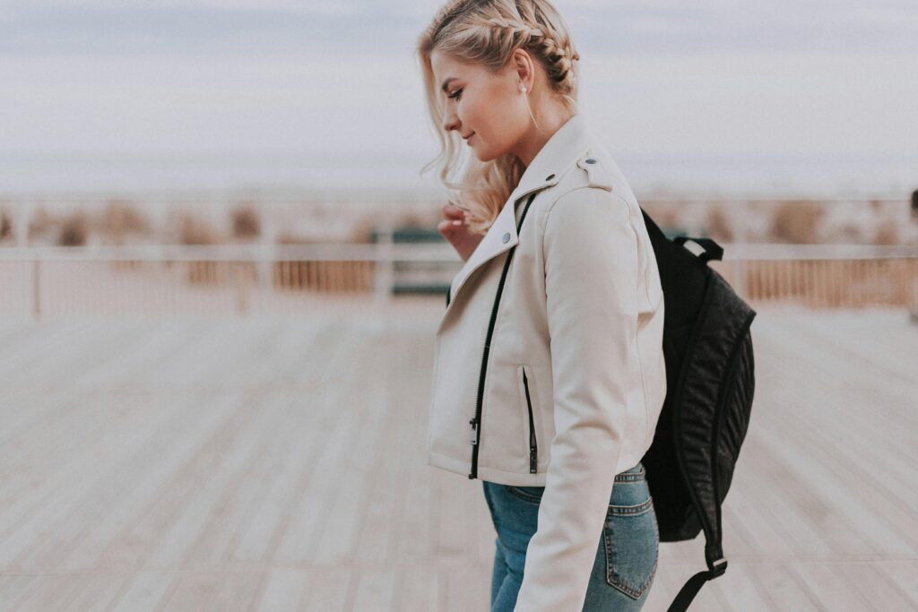 A young woman in a leather jacket walking on a boardwalk, embracing a casual and stylish vibe.