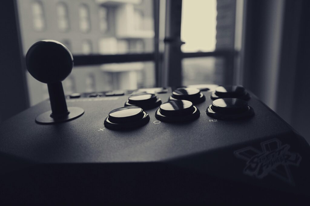 Black and white close-up of a retro gaming joystick with cityscape background.