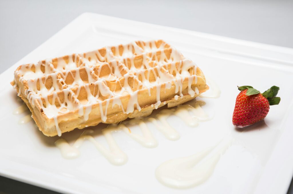 Delicious Belgian waffle drizzled with cream sauce and a fresh strawberry on a white plate.