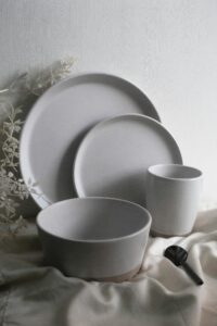 Elegant display of minimalist ceramic plates, bowls, and cup with foliage.