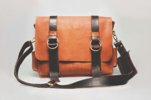 Elegant brown leather briefcase with dark straps and metal buckles, ideal for fashion and business.