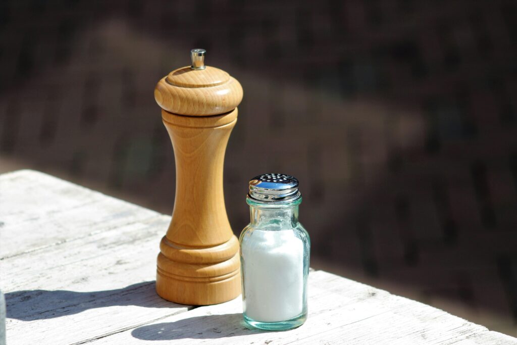Close-up of a wooden pepper mill and glass salt shaker on a rustic outdoor table.