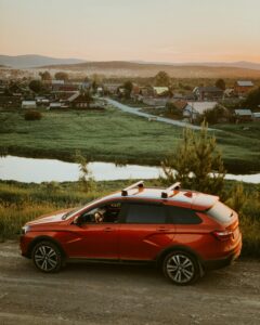 A red SUV on a dirt road with a rural village and river at sunset.