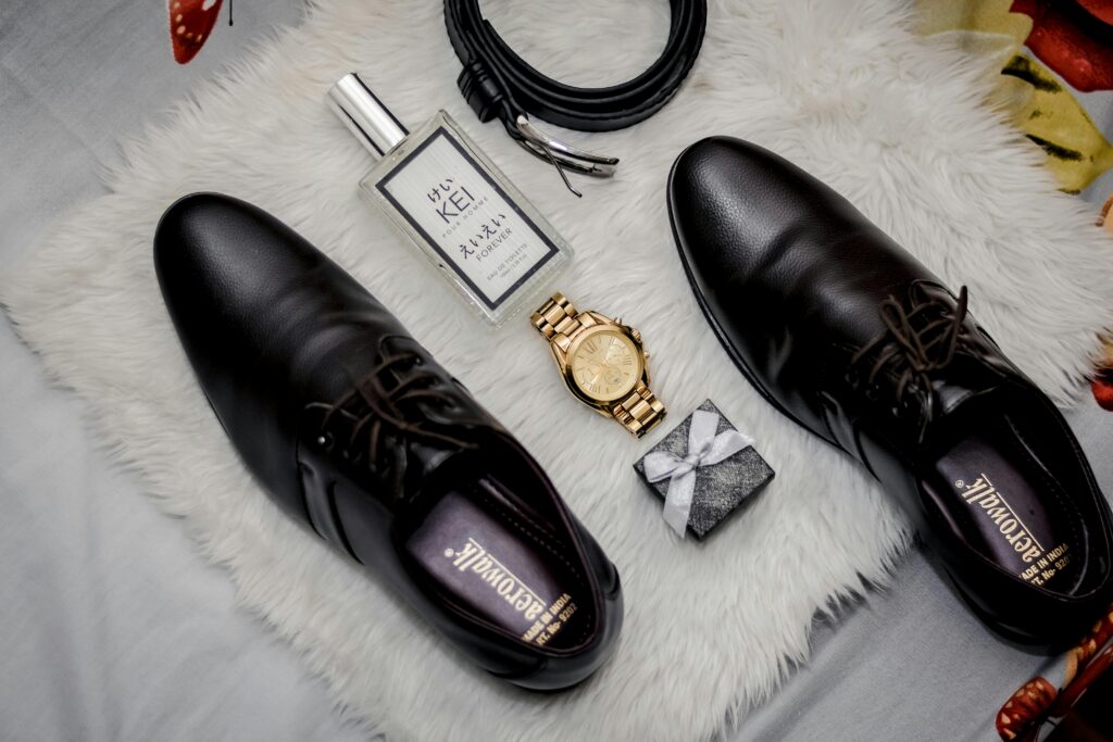 A stylish flat lay of men's fashion accessories featuring black leather shoes, a watch, and a gift box.