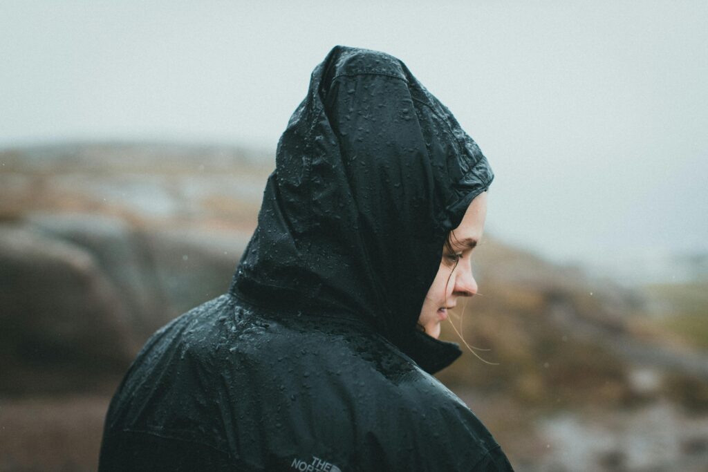 Side view of a woman in a rain jacket outdoors, experiencing rain with serene expression.