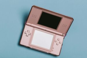 Close-up of a pink portable gaming console with dual screens on a blue surface.