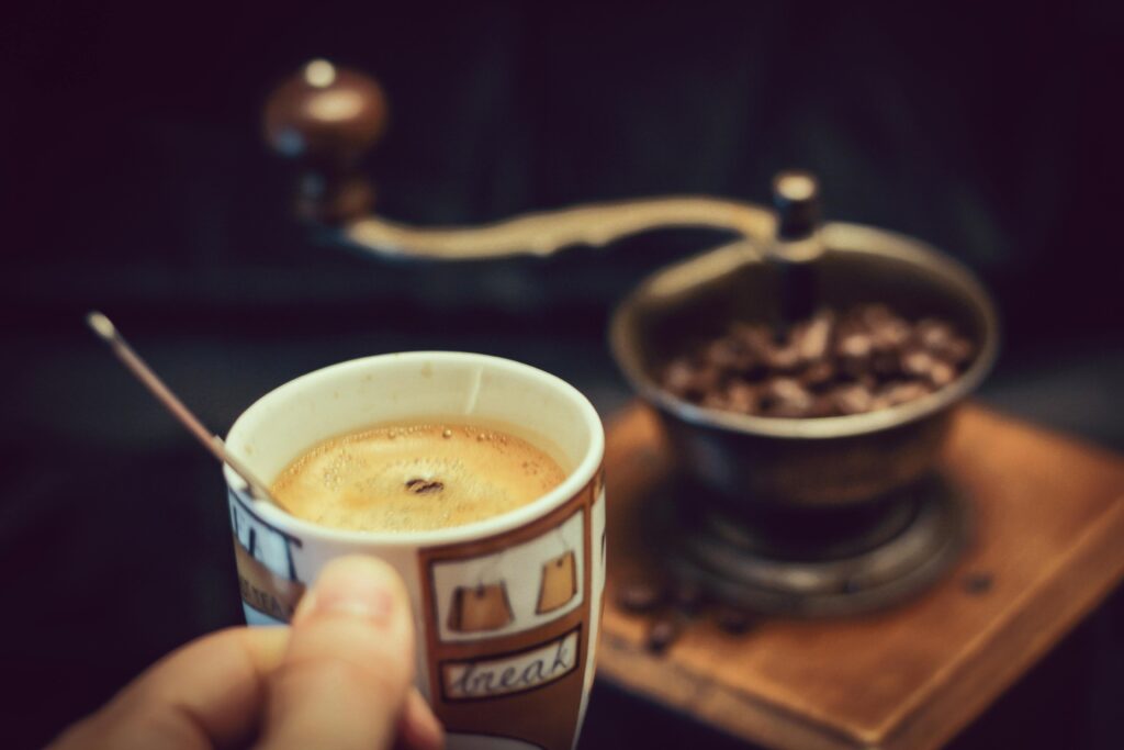Close-up of a steaming cup of coffee next to a vintage coffee grinder.