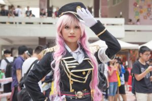 Young woman in detailed cosplay outfit saluting at an indoor event.