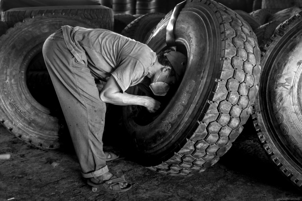 Monochrome photo showing a man working on large industrial tires indoors.