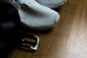 A close-up image of casual shoes and a leather belt on a wooden floor.