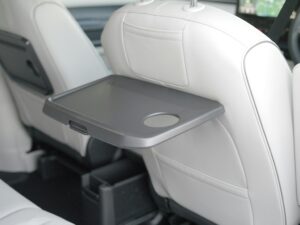 Inside view of a luxury car with white seats and a folding backseat table for comfort.