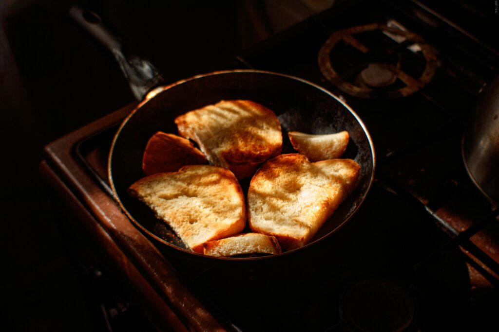 Golden brown toasts cooking in a skillet on a stovetop in warm lighting.