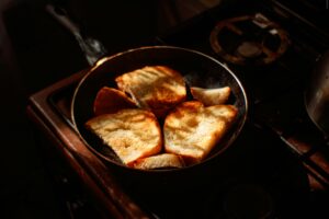 Golden brown toasts cooking in a skillet on a stovetop in warm lighting.