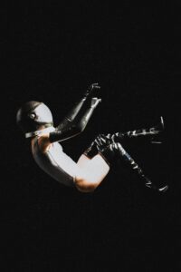 A woman astronaut in a helmet and black boots floating against a dark background.
