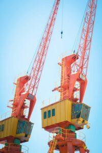 Two vibrant orange cranes under a clear blue sky, symbolizing modern industry and construction.
