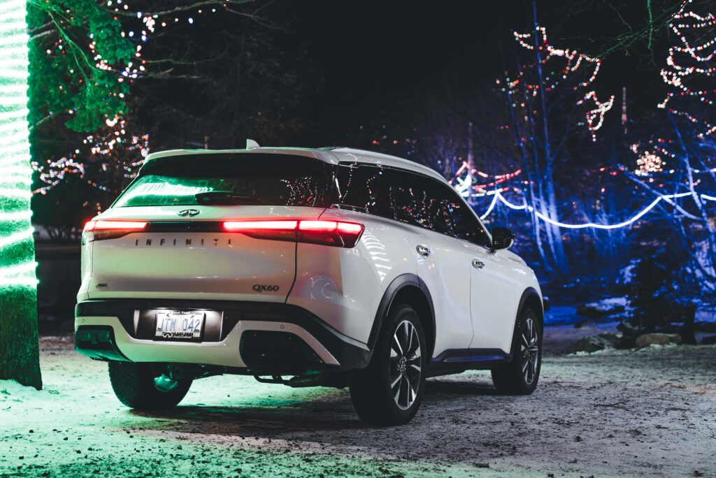 Elegant white Infiniti QX60 SUV parked amidst vibrant Christmas lights, creating a festive twilight ambiance.