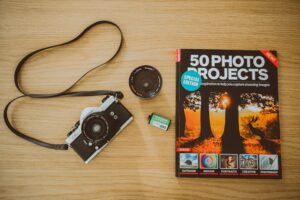 Vintage film camera with photography project book and accessories on wooden background.