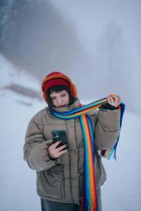 Woman in winter gear checks her phone, surrounded by snow and fog.