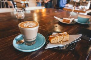 A latte with art and cake slice served on a wooden table in a cozy café environment. Perfect for coffee lovers.
