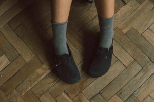 Close-up of a person wearing black sandals with blue socks on a wooden parquet floor.