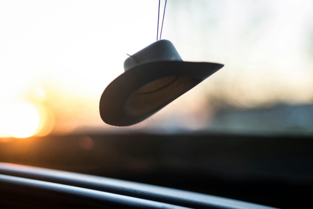 Minimalist silhouette of a hat hanging inside a car at sunset, capturing the warm light and travel vibes.