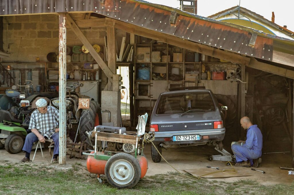 Mechanics fixing a car in a rural workshop in Parcoul-Chenaud, France. Captured traditionally.
