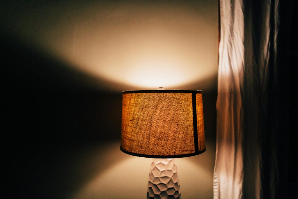 A rustic table lamp emits a warm glow in a cozy room with soft curtains.