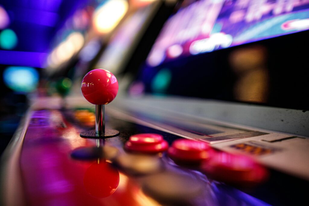 Close-up of a vibrant retro arcade joystick and buttons with blurred lights in the background.