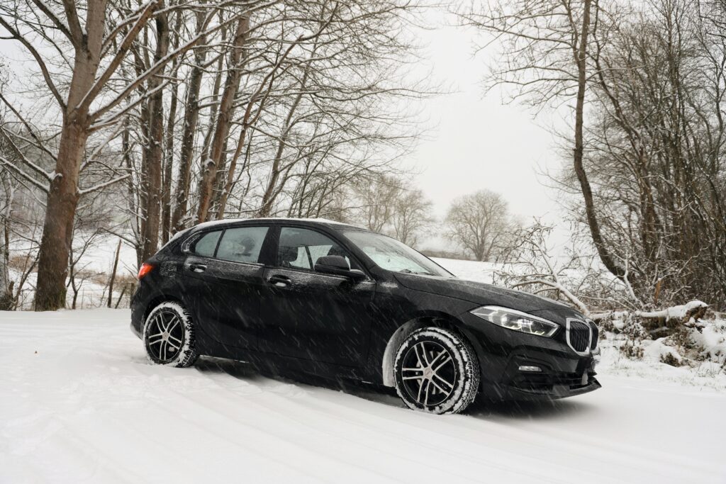 A black car driving through a snowy forest landscape, embodying winter weather's beauty.