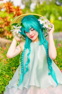 A cosplay character with blue hair and floral hat in a garden setting, evoking springtime.