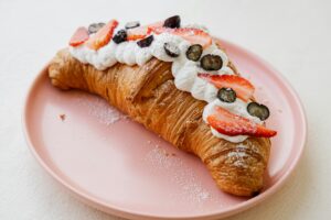 Croissant topped with fresh strawberries, blueberries, and whipped cream on a pink plate.